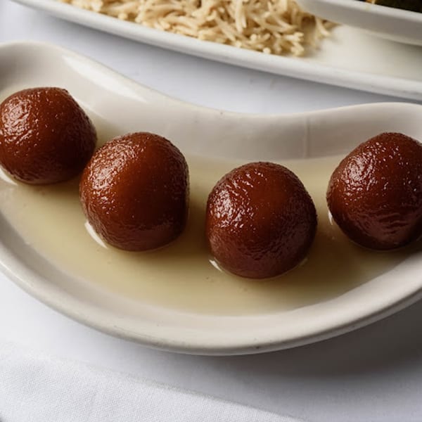 Four gulab jamun, Indian fried dough balls soaked in syrup, on a white dish.