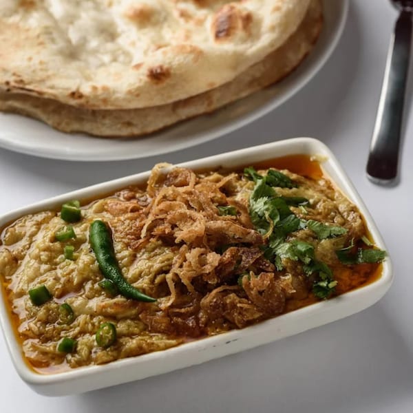 Indian baingan bharta with crispy onions, green chilies, and cilantro, served with naan bread.