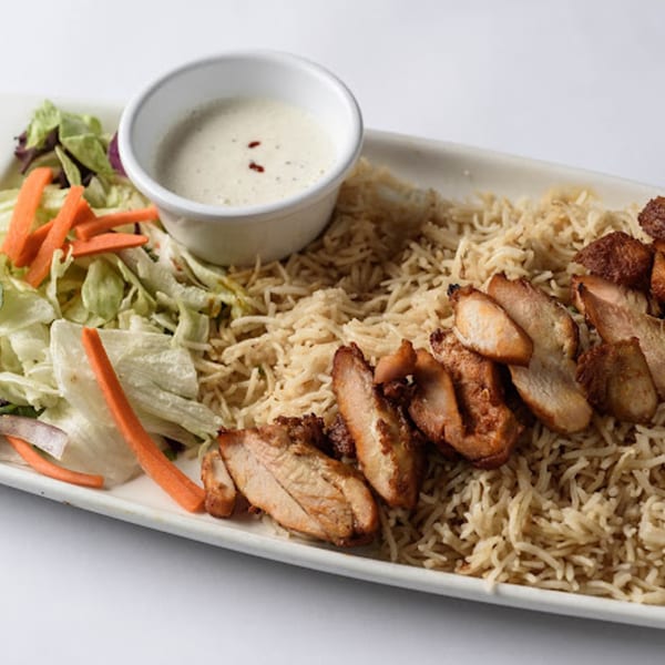 Indian chicken and rice dish with a side salad and white dipping sauce on a rectangular plate.