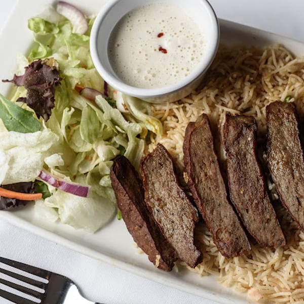 Indian dish with sliced meat, rice, a side salad, and a small bowl of white sauce.